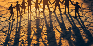 Silhouettes of paper-cut figures holding hands, casting long shadows on a textured surface in warm golden light, symbolizing unity and community.